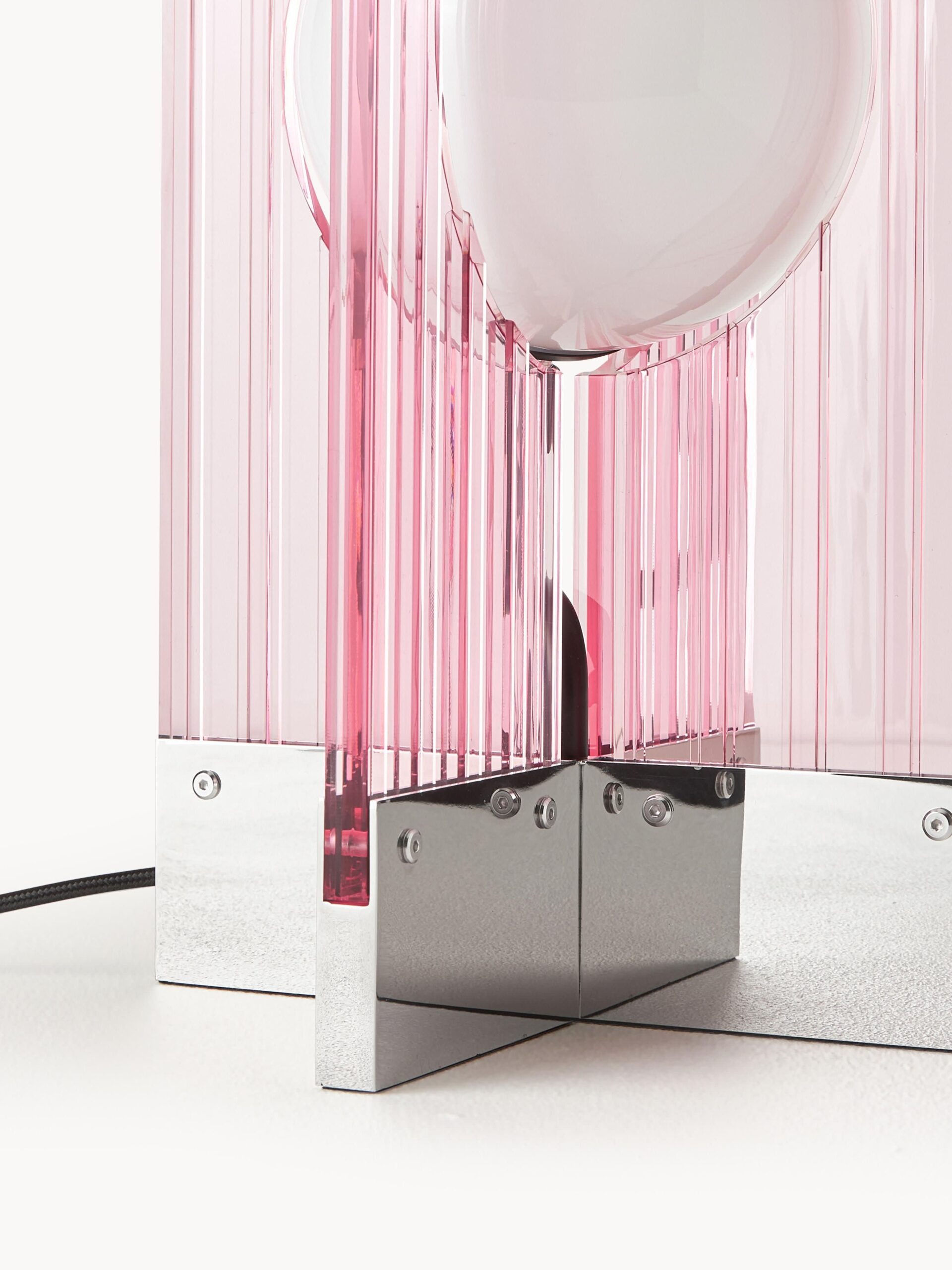 Šviesiai rožinio stalo šviestuvo Mills detalė: tekstūruotas stiklas, sidabrinis metalinis pagrindas, modernus retro dizainas.